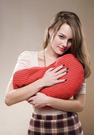Portrait of a  beautiful young brunette hugging red heart shaped pillow.の写真素材