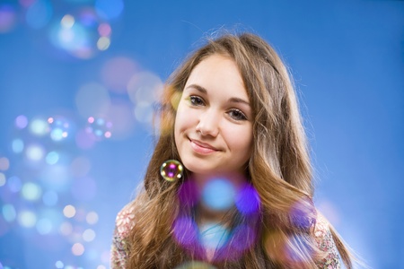 Portrait of a beautiful smiling young brunette girl among colorful soap bubbles.の写真素材