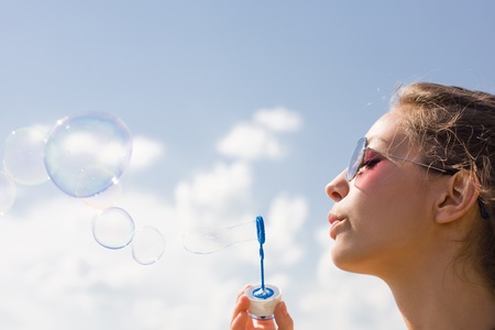 Beautiful young brunette woman blowing soap bubbles into blue sky.の写真素材