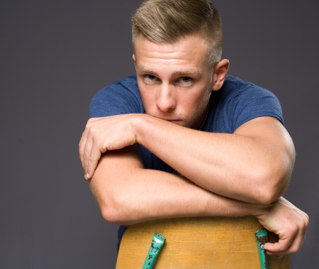 Attractive young blond man sitting on a chair pondering.の写真素材