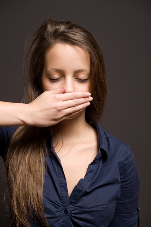 Dark moody portrait of young brunette woman with eyes closed and hand over mouth.の写真素材