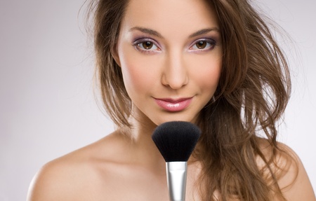 Portrait of a beautiful young brunette woman with makeup brush.の写真素材