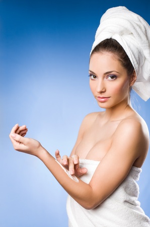 Portrait of a gorgeous brunette spa  woman using moisturizer on blue background の写真素材