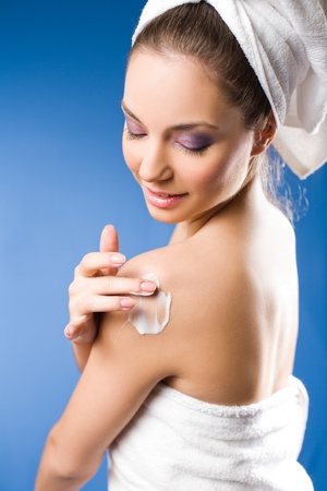 Portrait of a gorgeous brunette spa  woman using moisturizer on blue background の写真素材