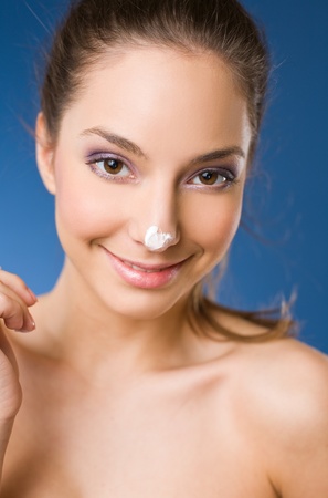 Cute young brunette woman pampering herself with body milk on blue background の写真素材