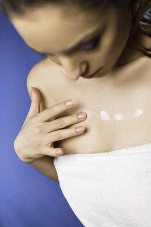 Portrait of a pretty young woman using body milk on blue background の写真素材