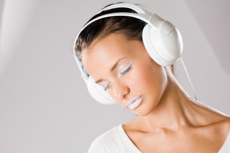 Dreamy young music lover, beautiful young brunette wearing big white headhones.の写真素材