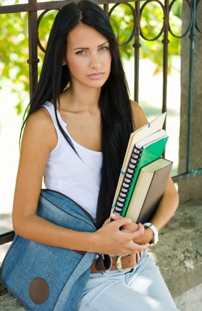 Portrait of a very tanned gorgeous young brunette student girl outdoors holding exercise books.の写真素材
