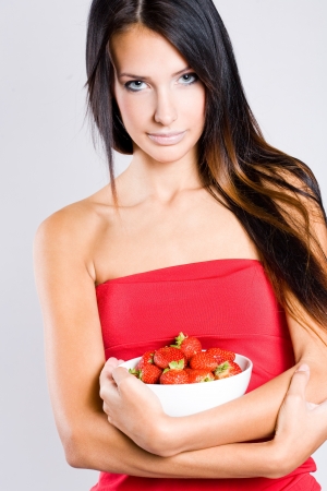 Portrait of a beautiful thin brunette with bowl of fresh strawberries.の写真素材