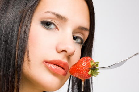 Closeup portrait of a gorgeous brunette with honey dripping strawberry.の写真素材