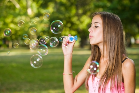 Portrait of a beautiful young girl blowing soap bubbles outdoors in the park.の写真素材