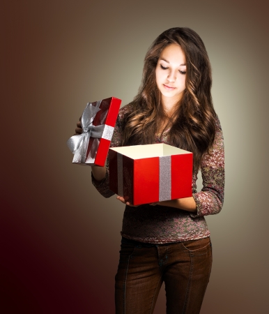 Portrait of a young brunette beauty with red gift box in creative lighting.の写真素材