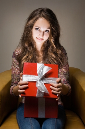 Portrait of a young brunette beauty with red gift box in creative lighting.の写真素材