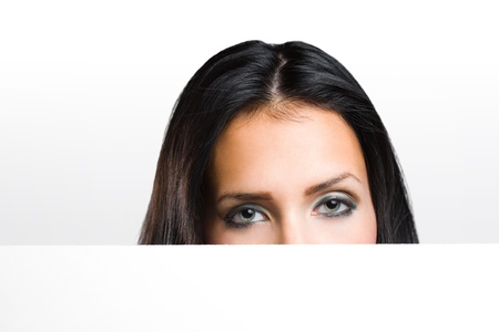 Portrait of a beautiful brunette peeking out from behind blank white banner.の写真素材