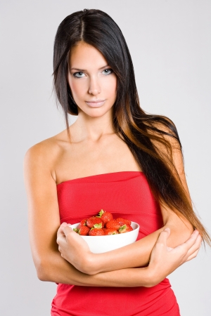 Portrait of a young brunette beauty with a bowl of fresh strawberries.の写真素材