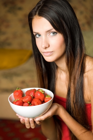 Portrait of a young brunette beauty with a bowl of fresh strawberries.の写真素材