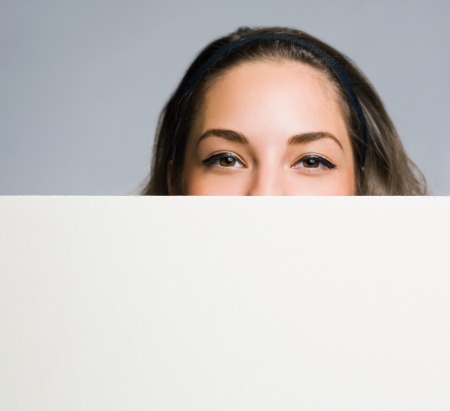 Beautiful young brunette woman peeking out from behind white empty baner.の写真素材