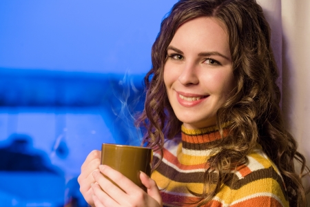 Portrait of a beautiful young brunette woman having a cozy drink for a cold evening.の写真素材