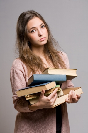 Portrait of wasted looking young student girl carrying large pile of books.の写真素材