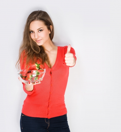 Portrait of a brunette beauty with bowl of strawberries showing thumbs up の写真素材