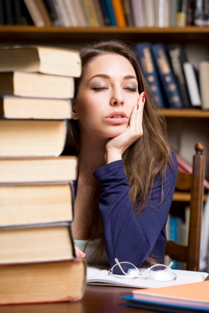 Portrait of an exhausted young brunette student woman with large pile of books の写真素材