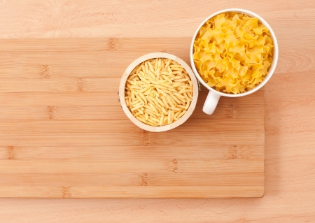Wooden and ceramic cups filled with tasyt pasta, on cutting board.の写真素材