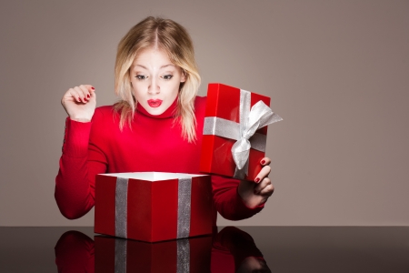 Portrait of a beautiful young blond woman holding shiny red gift box.の写真素材