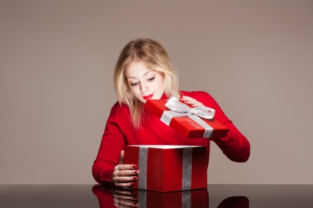 Portrait of a beautiful young blond woman holding shiny red gift box.の写真素材