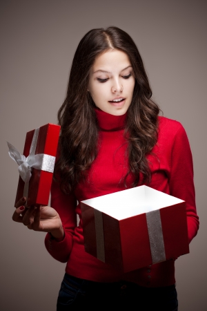 Portrait of an attarctive young brunette woman opening red christmas gift box in mysterious lighting.の写真素材
