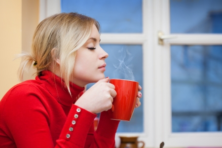 Gorgeous fashionable young blond woman relaxing with a cup of hot beverage の写真素材