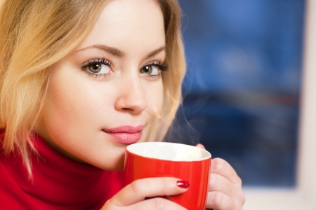 Gorgeous fashionable young blond woman relaxing with a cup of hot beverage の写真素材