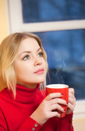 Portrait of a cute blond girl with a cup of hot beverage の写真素材