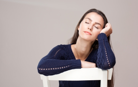 Portrait of a dreamy brunette woman on a white chair.