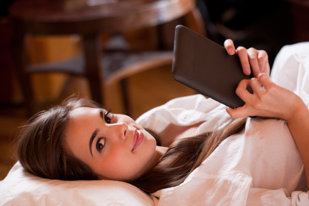 Beautiful young brunette doing some late night browsing on her tablet computer.の写真素材