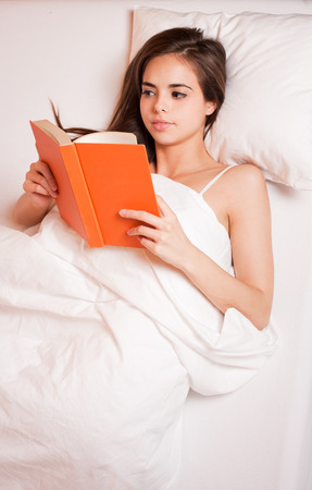 Gorgeous young brunette woman immersed in reading a book in bed.の写真素材