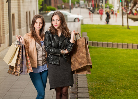 Couple of beautiful young brunette women with shopping bags outdoors.の写真素材