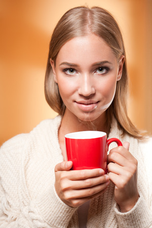 Beautiful young blond woman with mug of hot beverage.の写真素材