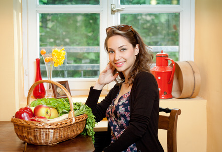 Gorgeous young brunette woman in the kitchen with basket full of healthy food.の写真素材