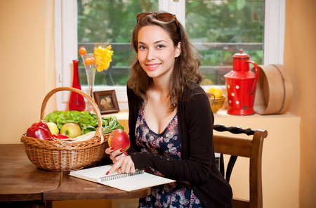 Young brunette beauty in the kitchen with large basket of vegetables and fruits.の写真素材
