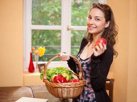 Young brunette beauty in the kitchen with large basket of vegetables and fruits.の写真素材