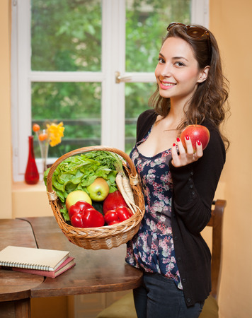 Gorgeous young brunette woman in the kitchen with basket full of healthy food.の写真素材