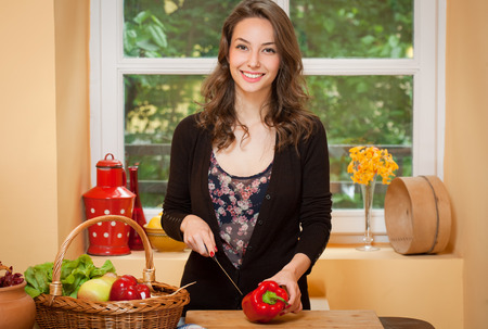 Young brunette beauty in the kitchen with large basket of vegetables and fruits.の写真素材