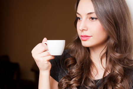 Closeup portrait of a gorgeous young brunette woman holding cup of coffee.の写真素材