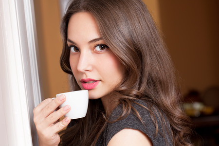Portrait of a gorgeous young brunette woman holding cup of coffee.の写真素材
