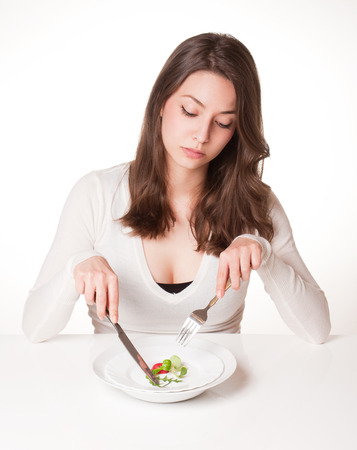Portrait of a frustrated looking young brunette woman with plate of vegetables.の写真素材