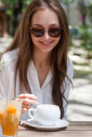 Stylish young brunette beauty having tasty refreshments in street coffee shop.の写真素材
