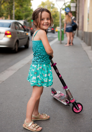 Cute young girl riding her scooter on city streets.の写真素材