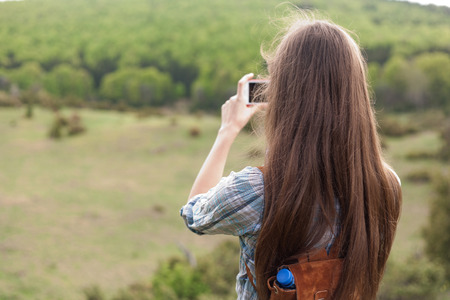 Young brunette woman using her smart phone to take home memories of hiking.
