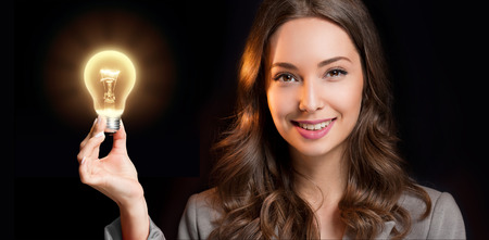 Gorgeous young businesswoman holding glowing light bulb idea symbol.の写真素材