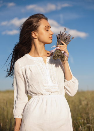 Portrait of a young brunette beauty enjoying the scent of lavender outdoors.の写真素材